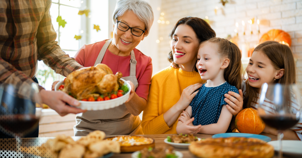 Family smiling around a holiday dinner table as an older woman serves a roasted turkey.